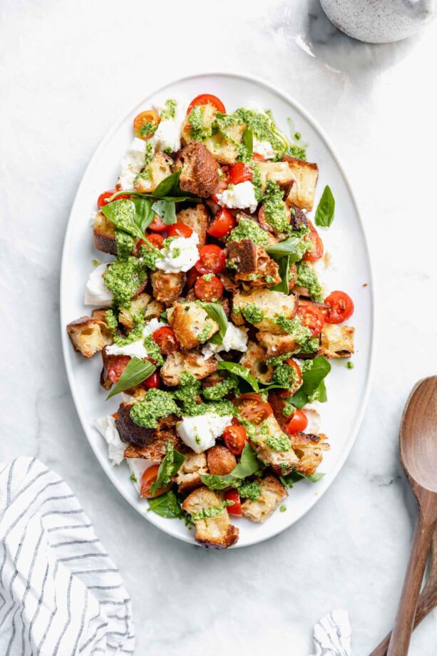 pesto caprese panzanella salad drizzled with pesto on a serving platter